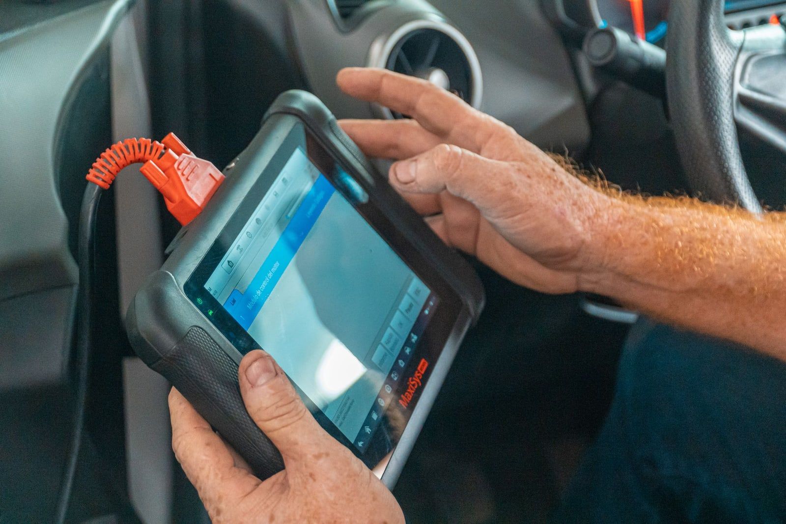 Manos con una tableta de diagnosis conectada a un coche
