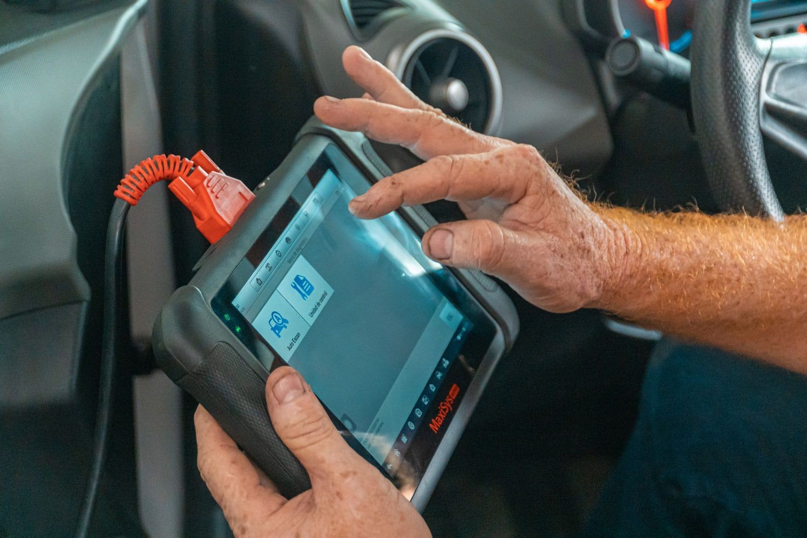 Manos manejando una máquina de diagnosis conectada a un coche