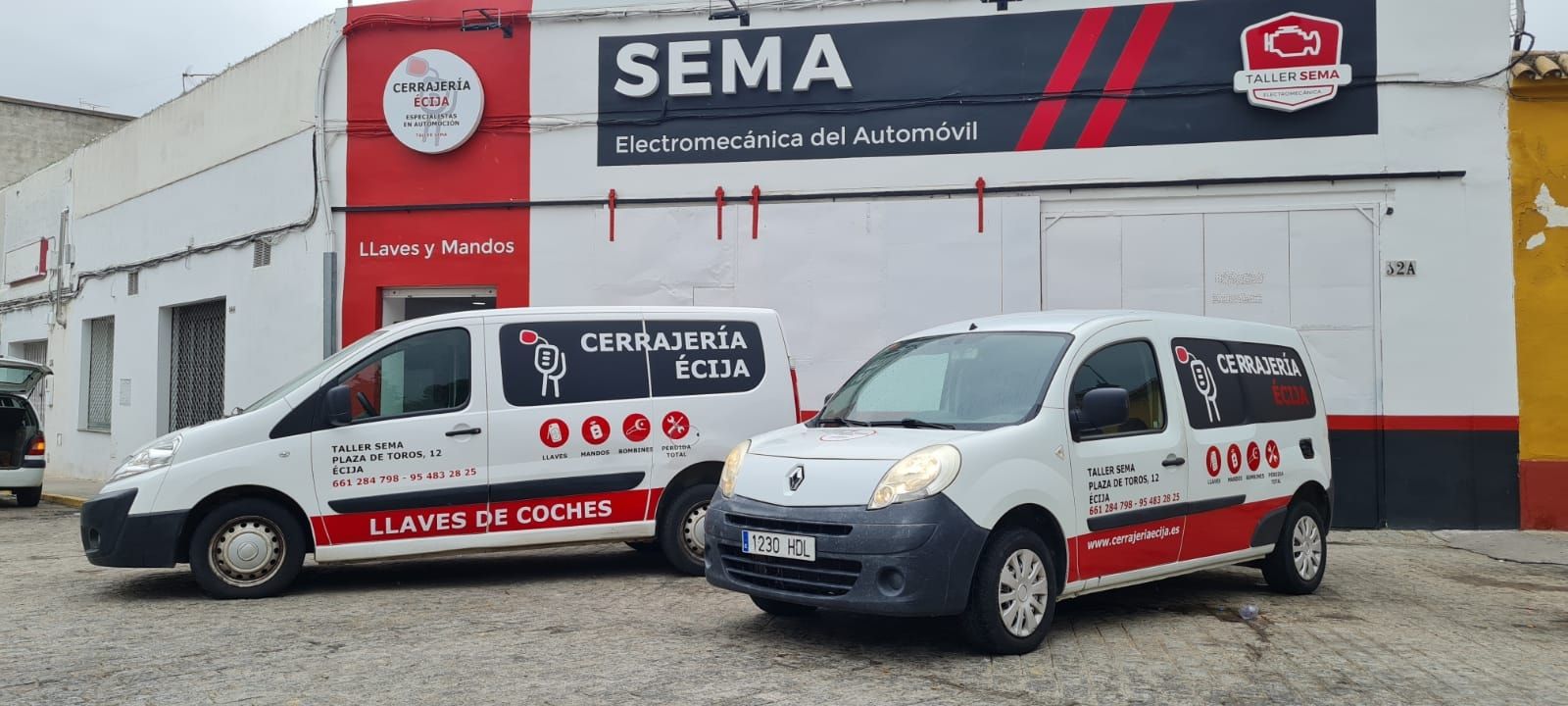 Fachada de Taller Sema en la Plaza de Toros de Écija, con el rótulo SEMA Electromecánica del Automóvil y dos furgonetas de Cerrajería Écija aparcadas delante